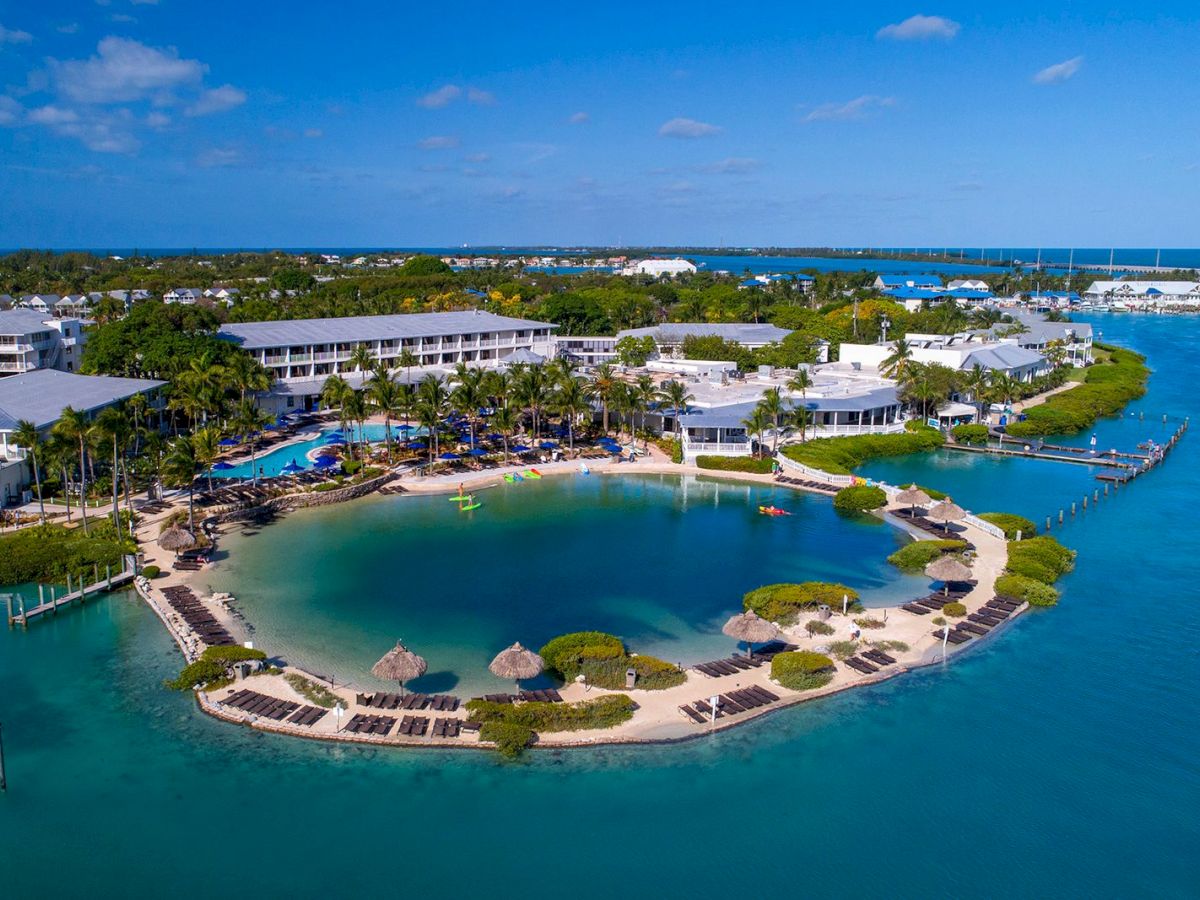 The image shows a coastal resort with buildings, pools, and a lagoon surrounded by sandy beaches, lounge chairs, and tropical landscaping, ending the sentence.